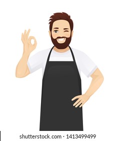 Handsome man in black apron gesturing ok sign isolated vector illustration
