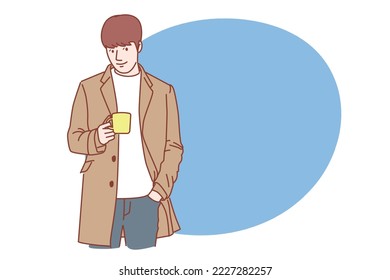 
Handsome young man wearing a coat drinking coffee happily.
