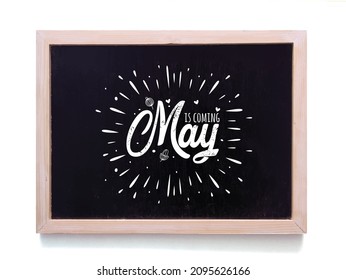 Handwritten text May is coming  black chalkboard againt white outdoor wall
