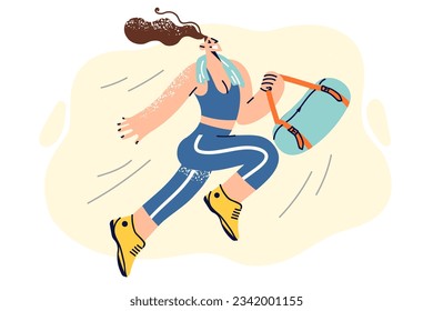 Happy athletic woman in sportswear holding bag with workout accessories and running to fitness club. Girl with towel around neck is returning from gymnastics or aerobics classes in fitness studio