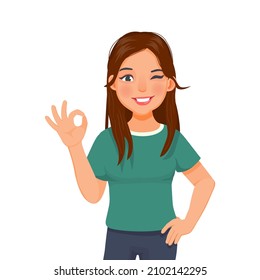 Happy beautiful young woman giving well done ok sign with winking eye and positive feedback approval standing with hand on the waist looking confident smiling expression