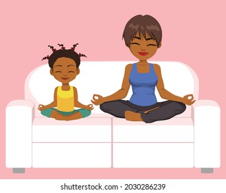 Happy black mother and daughter family meditating and practicing yoga exercises sitting on comfy white couch in lotus position having fun together