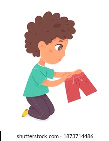 Happy boy sitting holding red shorts. Joyful little child sitting on floor. Positive emotion vector illustration. Cute cheerful small kid with clothes in hands on white background.