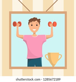 Happy Boy Standing Training with Red Dumbbell.. View Photo Young Smiling Child Holding his Hand Up with Dumbbell who won Prize Competition. Champion Cup. Frame under Photo Hanging on Wall