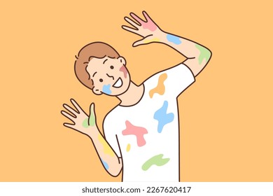 Happy boy with traces of paint on clothes and face after drawing lesson at school. Cheerful schoolboy in white t-shirt smeared with multi-colored paint looks at camera