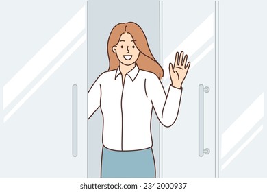 Happy business woman stands at door of business center, says welcome and waves hand inviting you to visit corporate office. Positive girl office employee says goodbye to colleagues before leaving