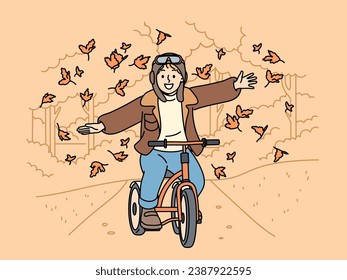 Happy child rides bicycle through autumn park and spreads arms to sides enjoying good weather and falling leaves. Cheerful boy cyclist takes airplane pose riding bicycle along autumn streets