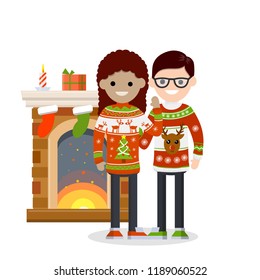 A happy couple family in winter sweaters with a pattern stands next to the fireplace with boxes of gifts and candles. New year and Christmas celebration.
