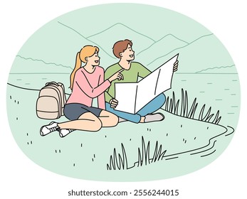 Happy couple of travelers sitting on lawn during hike in national park with lake and holding map in hands. Cheerful man and woman went on hike for adventure and new positive emotions