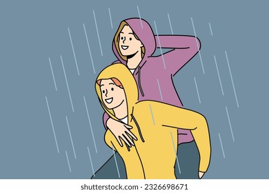 Happy couple walks in rain enjoying downpour after long drought and not wanting to go home. Man in waterproof hood rolls laughing girlfriend on back and enjoys autumn weather with rain