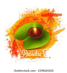 Happy Dussehra Lettering With Burning Oil Lamp (Diya) Over Betel Leaf And Orange Brush Splash On White Background.