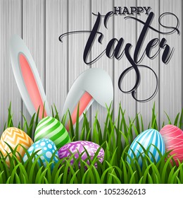 Happy Easter background with colored eggs and ears bunny in the grass on wooden background
