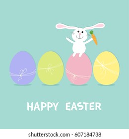 Happy Easter bunny. Rabbit with carrot sitting on painting egg shell set. Painted eggs with thread and bow. Farm animal. Cute cartoon funny character. Greeting card Blue background. Flat design Vector
