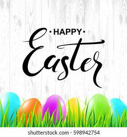 Happy Easter handwritten calligraphy lettering with colorful eggs and grass on wood texture background. Vector illustration.