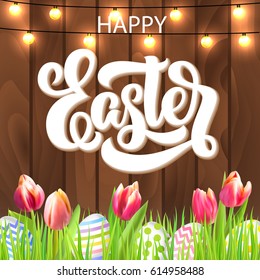 Happy Easter lettering with eggs, garland and tulip flowers in grass on rustic wooden background. Festive vector design. 