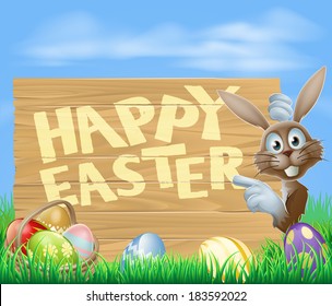 Happy Easter sign with Easter bunny pointing at the wooden sign with the message Happy Easter written on it. Chocolate eggs and basket in the foreground.