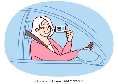 Happy elderly woman demonstrates driver license sitting behind wheel of car and rejoices at opportunity to go on road trip. Positive grey-haired old lady got driver ID after retirement