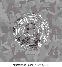 happy face icon inside grey camouflaged emblem