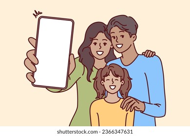 Happy family holds phone with blank screen in hands, offering to use advertising mobile application. Mom, dad and daughter are laughing demonstrating phone with place for ads website