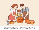 Happy family makes halloween pumpkins to decorate house for october 31st and celebrate all saints day. Boy together with parents, dressed in aprons, cuts out jack-o-lanterns for celebration halloween