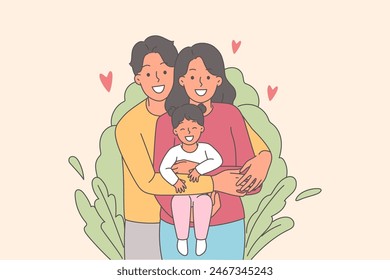 Happy family of mom and dad with little girl in arms, standing near bush and with smile looking at camera. Young couple with child celebrate family day and enjoy spending time together