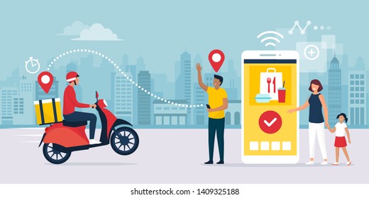 Happy family standing next to their smartphone in the city street, they are receiving a ready fast food meal ordered online using a mobile app, the delivery man is riding a moped