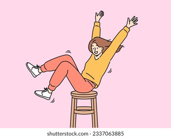 Happy girl is spinning on wooden chair, raising hands up and sharing good mood with others. Positive teenager girl in stylish clothes enjoys life without wanting to pay attention to troubles