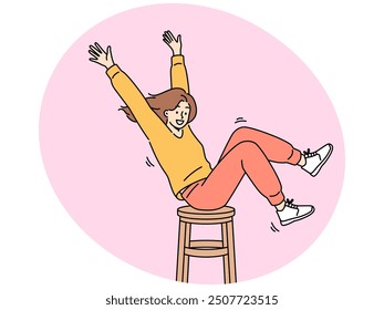 Happy girl is spinning on wooden chair, raising hands up and sharing good mood with others. Positive teenager girl in stylish clothes enjoys life without wanting to pay attention to troubles