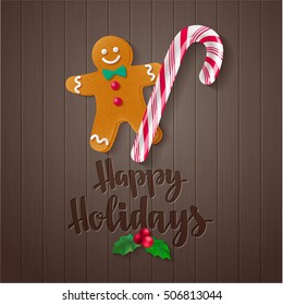 Happy Holidays. Holiday greeting card with calligraphy and decorative elements. Handwritten modern lettering with candy cane, holly and gingerbread man on dark wooden background.