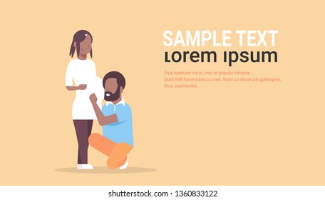 happy husband on knee listening his pregnant wife belly african american couple man woman young family pregnancy parenthood concept full length horizontal copy space