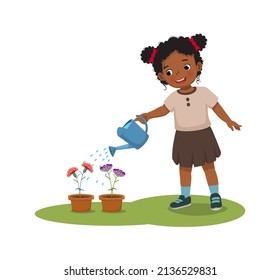 happy little African girl watering plants flowers in the pot with watering can in the garden