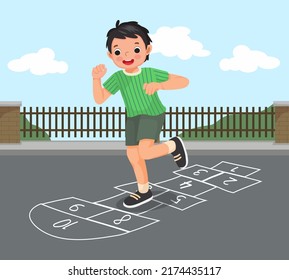 happy little boy playing hopscotch drawn with chalk outside on playground street at the park