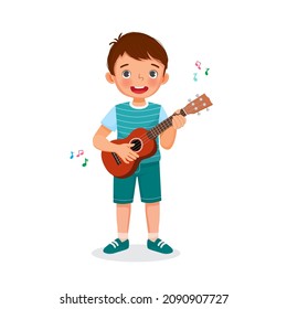 Happy little boy playing ukulele singing holding guitar with smiling facial expression