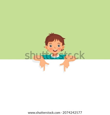 Happy little boy standing behind blank board peeking and pointing finger on empty banner. 