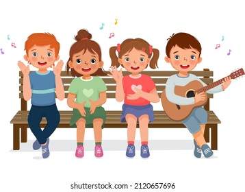 happy little boys and girls clapping hands, singing, playing guitar and having fun together sitting on bench