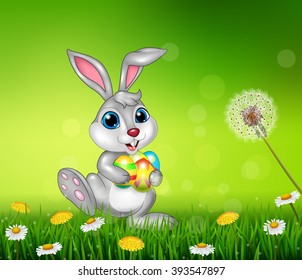 Happy little bunny holding easter eggs on grass background