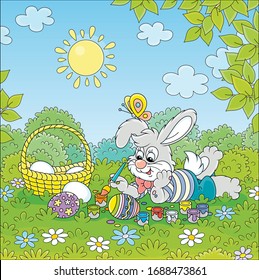 Happy little bunny painting and decorating Easter eggs with bright and colorful paints and a paintbrush on green grass of a pretty forest glade on a sunny spring day, vector cartoon illustration