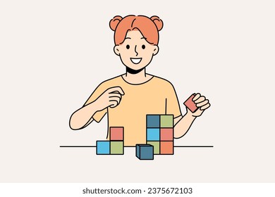 Happy little girl playing with wooden child cubes standing at table and smiling looking at screen. Child plays educational game that helps improve intellectual abilities and fine motor skills.