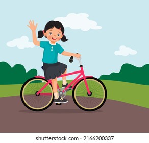 happy little girl riding a bike having fun in the park sunny day waving hand