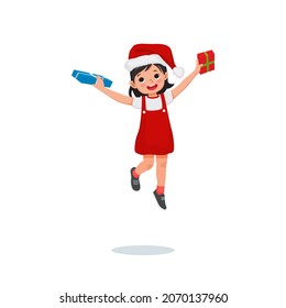 Happy little girl in Santa hat jumping while holding gift box feeling excited receiving Christmas present.  