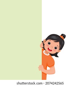 Happy little girl standing behind blank board peeking and pointing finger on empty banner. 