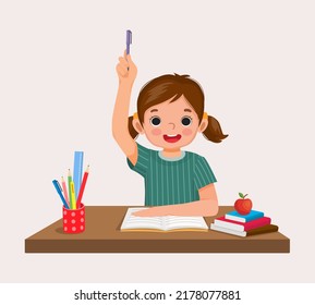 happy little girl student rising hand answering question sitting at her desk in the classroom