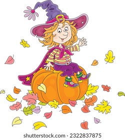 Happy little Halloween witch with a big hat and a cloak with stars sitting on a large orange pumpkin and waving in greeting among colorful autumn leaves, vector cartoon illustration