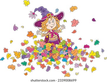 Happy little witch friendly smiling, playing with colorful fallen autumn leaves and tossing them up, vector cartoon illustration isolated on a white background