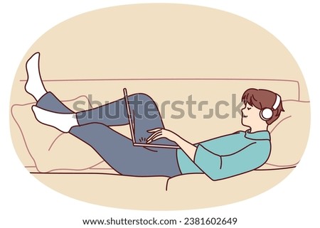 Happy man lying on couch wear headphones work on laptop. Smiling guy relax on sofa at home listen to music in earphones using computer. Vector illustration.