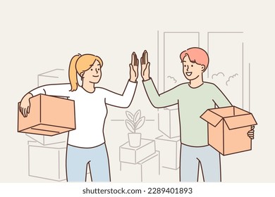 Happy married couple moving into new house and giving each other high five standing with boxes in hands. Man and woman rejoice in moving and renting good property or profitable mortgage