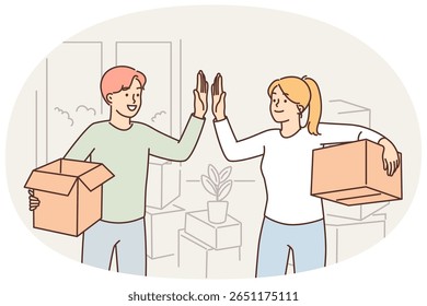 Happy married couple moving into new house and giving each other high five standing with boxes in hands. Man and woman rejoice in moving and renting good property or profitable mortgage