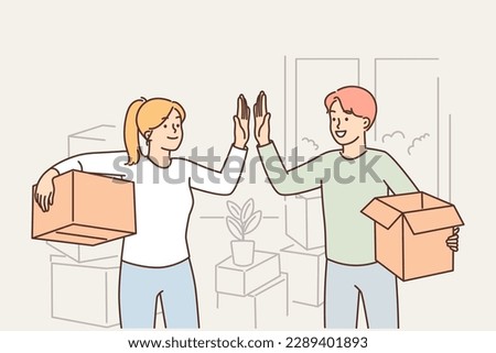Happy married couple moving into new house and giving each other high five standing with boxes in hands. Man and woman rejoice in moving and renting good property or profitable mortgage