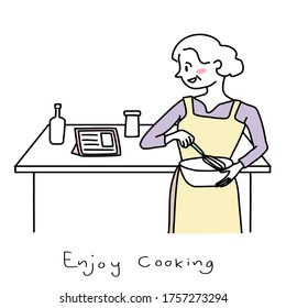 Happy mature woman whisking batter while looking recipe in tablet. Cute senior woman stirring batter in a mixing bowl. Cheerful woman reading food recipe in tablet and cooking meal from the recipe.