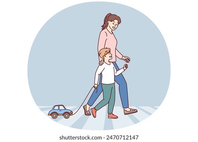 Happy mom and child going along pedestrian crossing across road walking through summer city. Little boy with toy car walks with nanny teaching how to cross intersection road correctly